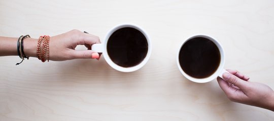 two hands holding two cups of coffee